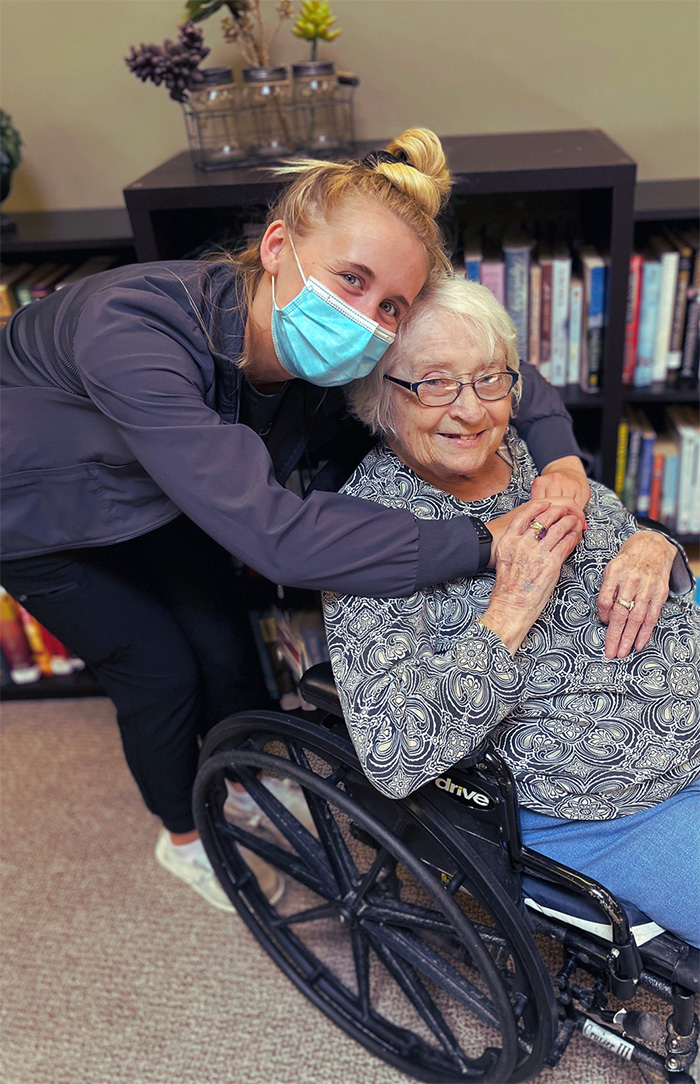A nurse leans over and hugs a resident seated in a wheelchair at Auburn Homes