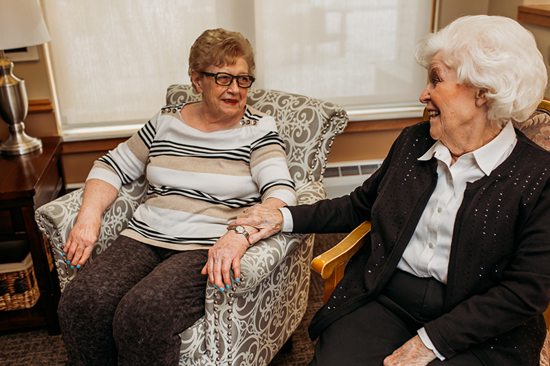 Two residents at Auburn Courts in Chaska chat and touch arms 